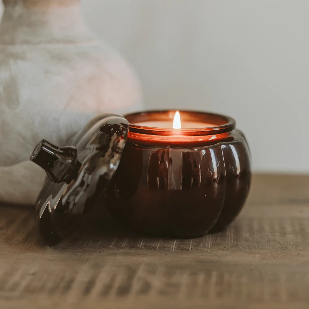 Lit amber pumpkin-shaped candle on a rustic table beside a cozy sofa